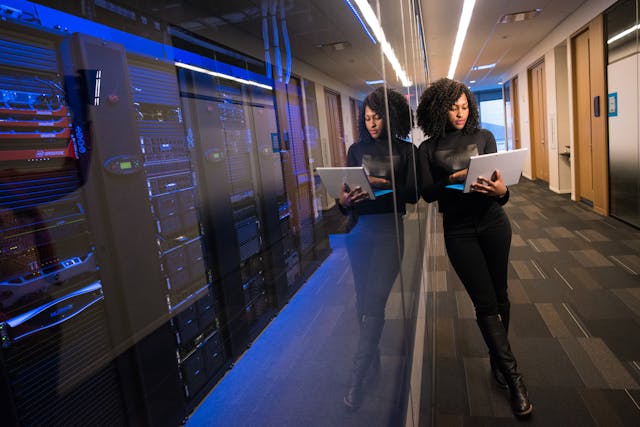 A cover photo for the blog post, a woman engineer holding a laptop standing next to datacenter